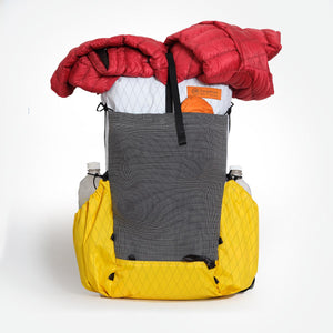 Ultralight hiking backpack OB30 made by OrangeBrown in yellow/white. With a full main compartment, water bottles in side pocket and puffy jacket strapped over the top ready for a hike.