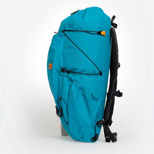 Side view of backpack OB 36 with side pocket and compression cords visible. Made from teal VX21