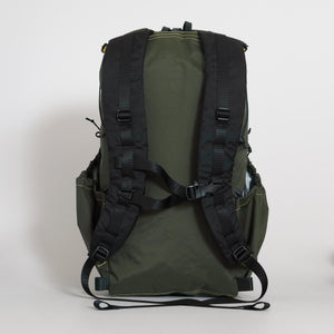 The back view of a dark green UL hiking backpack, showing the padded shoulder straps, sternum strap with emergency whistle and two large side pockets.