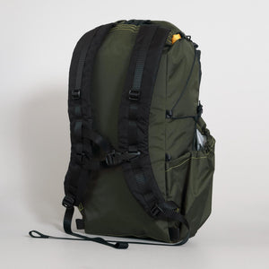 A dark green backpack with black shoulder straps, buckles, and trim made from X-Pac VX21 fabric. Shown from a three-quarters angle against a light gray background.