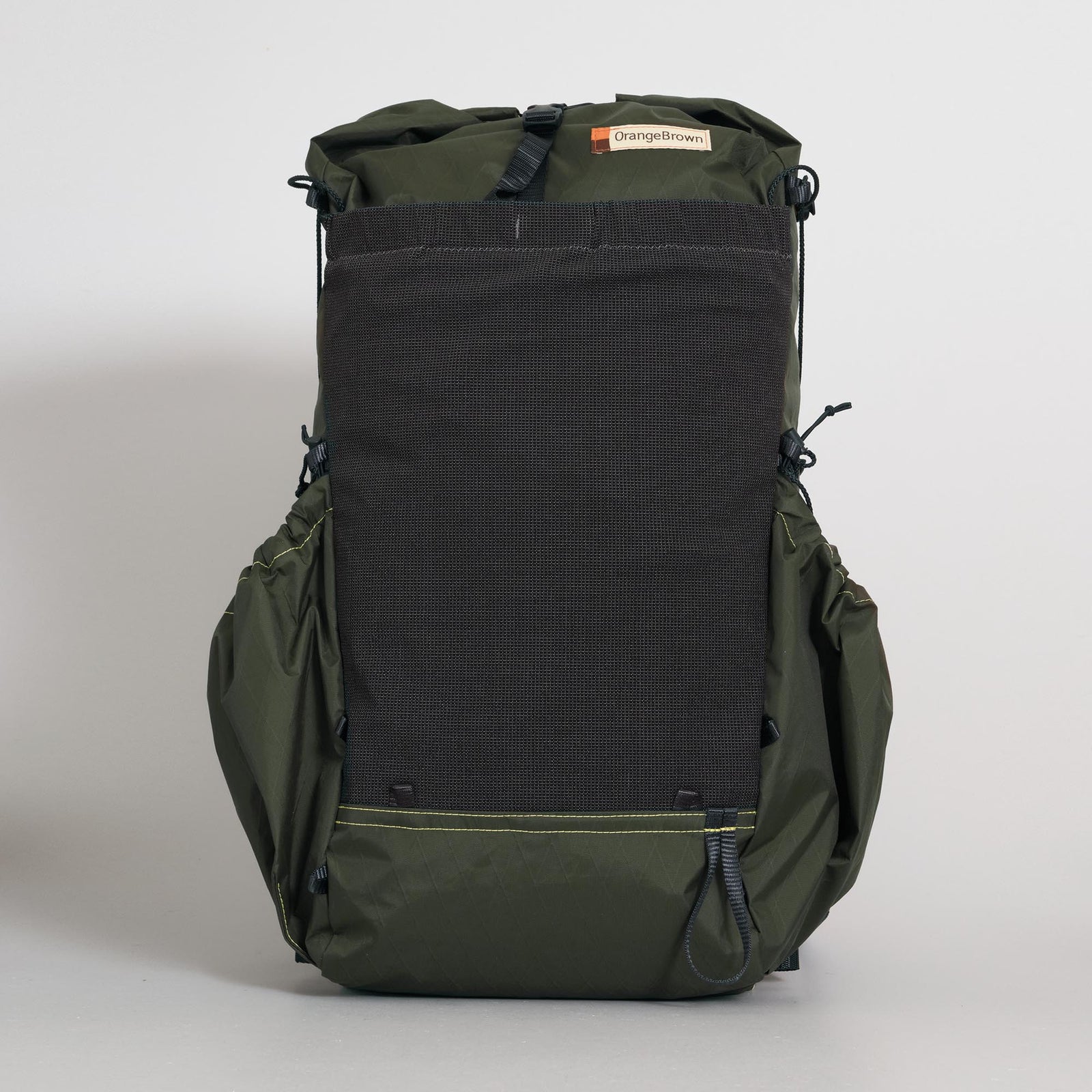 A dark green roll-top backpack with a front stretch mesh pocket, solid fabric side pockets, and a roll top closure. Handmade from X-Pac VX21 fabric in Australia. Photographed against a neutral light gray background.