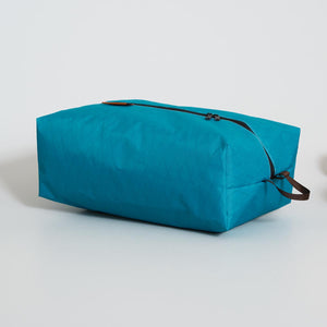 Teal toiletry bag with black zippers on a light gray background.