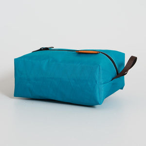 Blue toiletry bag with brown handle on a light gray background