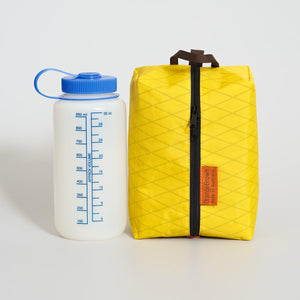 Yellow packing cube, packing cell for travel and hiking. A one liter water bottle next to it for size comparison