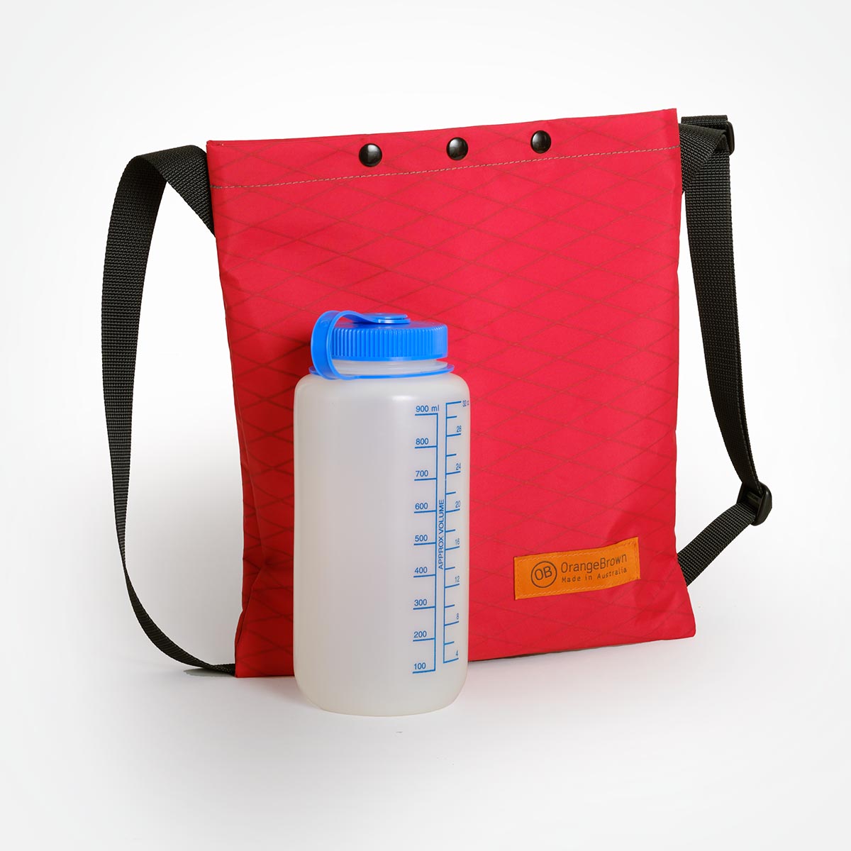 A red sling bag made by OrangeBrown in Australia from X-Pac VX21 fabric with  a Nalgene 1L bottle in size comparison.