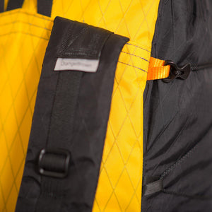 Detail view of a LineLoc 3 with a black 2.5mm cord running through it for the compression of a backpack. LineLoc3 is hold in place by an orange webbing loop.